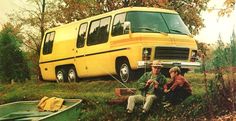 two people sitting in the grass next to a yellow bus and a small green boat