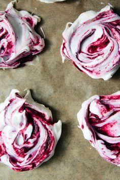 four cupcakes with white frosting and red swirled icing on top are sitting on a piece of parchment paper