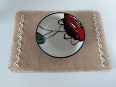 a white plate with a red flower on it sitting on top of a place mat