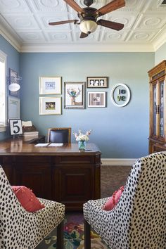 two chairs in front of a desk with pictures on the wall behind them and a ceiling fan