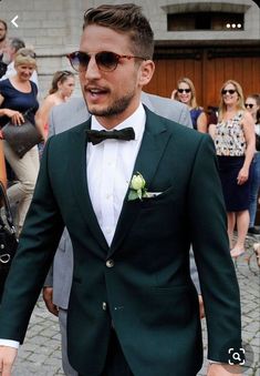 a man in a suit and bow tie walking down the street with people behind him