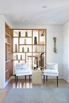 two white chairs sitting in front of a wooden shelf filled with vases on top of it