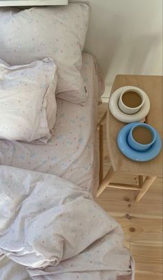 a bed with white sheets and pillows next to a cup of coffee on a small table