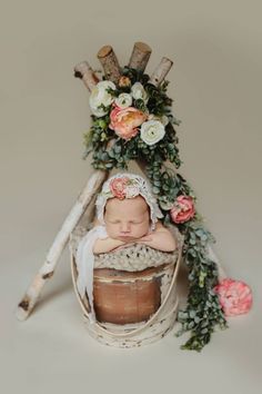 a baby is sleeping in a basket with flowers on the top and branches around it