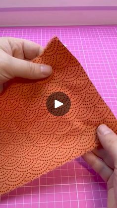 someone is cutting out an orange piece of fabric on a pink surface with a video screen