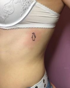 a small penguin tattoo on the side of a woman's stomach is seen in this image