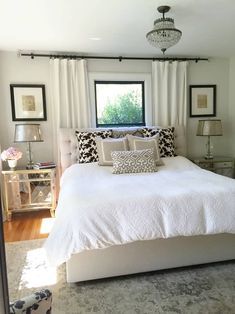 a white bed sitting in a bedroom next to a window with curtains on the windowsill