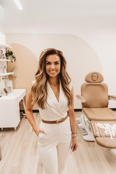 a woman standing in front of a chair with her hands on her hips and smiling at the camera