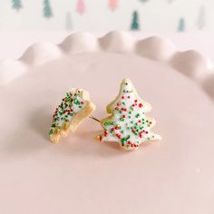 two decorated cookies sitting on top of a white cake plate with frosting and sprinkles