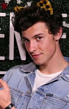 a young man with a flower in his hair is looking at the camera while wearing a denim jacket