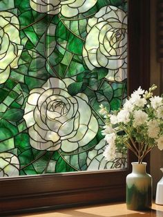 a vase filled with white flowers sitting next to a stained glass window covered in green leaves