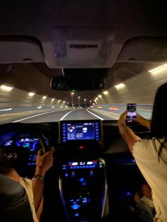 two people in a car driving down a highway at night with their cell phones up