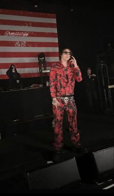 a man in red and black outfit standing on stage with an american flag behind him