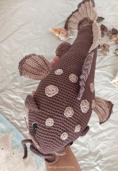 a crocheted stuffed fish on top of a plastic sheet with shells around it