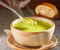 a wooden bowl filled with green soup on top of a plate next to some bread