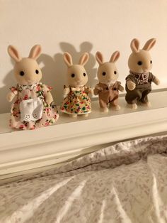 three little stuffed animals sitting on top of a white shelf next to a bed and wall