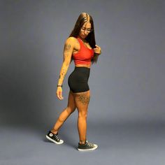 a woman in black shorts and a red top is posing for the camera with her hands on her hips