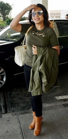 a woman is walking down the street with her hand on her head and wearing sunglasses