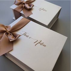 two white boxes with brown bows tied around the top and bottom, one has a name on it