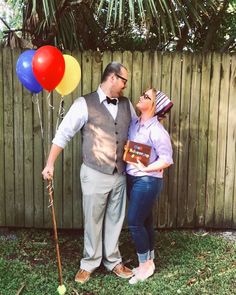 a man and woman standing next to each other in front of a fence with balloons