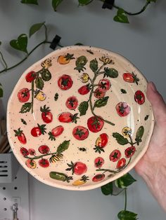 a hand holding a bowl with tomatoes painted on the bottom and green leaves around it