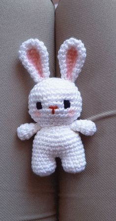 a crocheted white bunny sitting on top of a gray couch next to a pillow