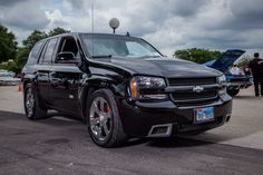 a black truck is parked in a lot with other cars and people standing around it