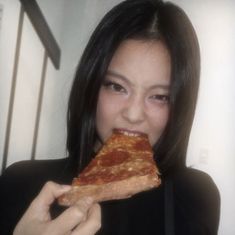 a woman eating a slice of pizza in front of her face and looking at the camera