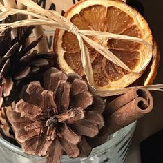 an orange, pine cone and cinnamon stick in a glass container with some dried fruit