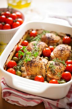 a casserole dish filled with chicken, tomatoes and fresh herbs next to a bowl of cherry tomatoes