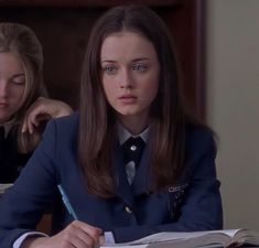 two women sitting at a table with pens and paper in their hands, one is writing