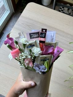 a person holding a paper bag with flowers and cosmetics in it on top of a table