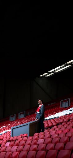 a man is standing in the middle of a stadium with red seats and an empty podium