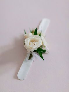 a boutonniere with white flowers and greenery on the top is laying on a pink surface