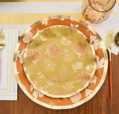 an orange and gold plate with leaves on it sitting on top of a wooden table