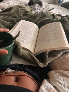 a person laying in bed reading a book and holding a cup with their hands on top of the book