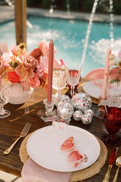 the table is set for an elegant dinner by the pool with pink flowers and candles