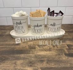 three cups filled with marshmallows, crackers and chocolate on a tray