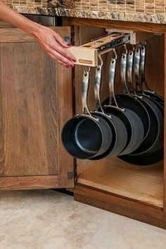 a person is holding pots and pans in a kitchen cabinet with wooden drawers on both sides