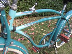 a close up of a blue bicycle parked in the grass with leaves on the ground