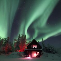 the aurora bore is shining brightly in the sky above a cabin on a snow covered hill