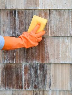 a person in orange gloves and rubber gloves is cleaning a wooden wall with a sponge