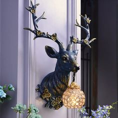 a deer head mounted to the side of a building with a light bulb hanging from it's antlers