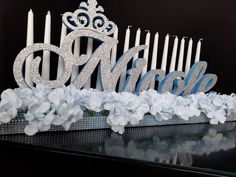 a table with candles, flowers and a tiara on top of it in front of a black background