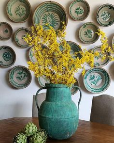 a green vase with yellow flowers sitting on a table in front of plates and bowls