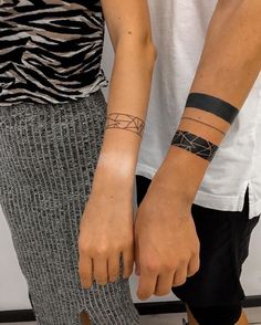 two people holding hands with tattoos on their arms and one has a wristband in the other hand