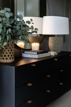 a black dresser topped with a vase filled with green plants and two lit candles on top of it