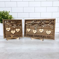 two wooden signs with hearts hanging from them on a white table next to a potted plant