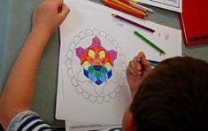 a young boy is drawing on paper with colored pencils