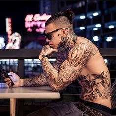 a tattooed man sitting at a table looking at his cell phone